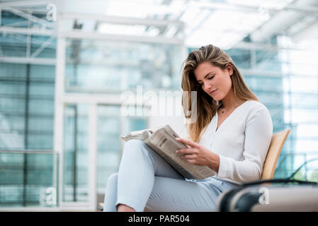 Junge Geschäftsfrau, Sitzen im Freien mit Koffer lesen Zeitung Stockfoto