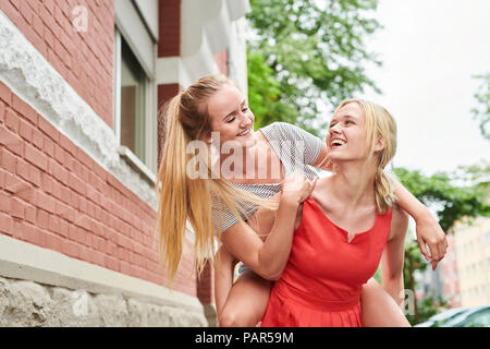 Glückliche junge Frau, Freund piggyback Ride in der Stadt Stockfoto