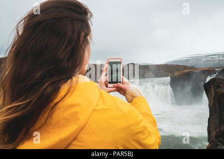 Island, Frau unter Handy Bild der Godafoss Wasserfall Stockfoto