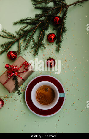 Leckere, frische Morgen winter festliche Espresso in eine grüne Tasse und Untertasse rot auf dem grünen Hintergrund mit Weihnachten Dekoration Stockfoto