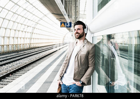 Lächelnden jungen Mann mit Kopfhörern am Bahnsteig warten Stockfoto
