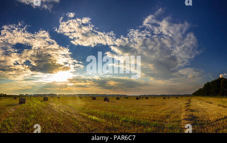 Dramatischer Sonnenuntergang über die Felder. Strohballen in Felder Ackerland mit blauen bewölkten Himmel bei der Ernte. Feld in der unglaublich schönen bunten Sommer Stockfoto