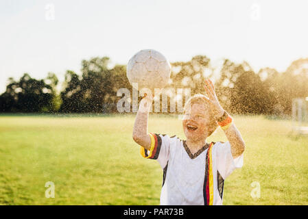 Junge tragen Deutsche Fussball shirt schreien vor Freude, stehend im Wasser spritzt Stockfoto