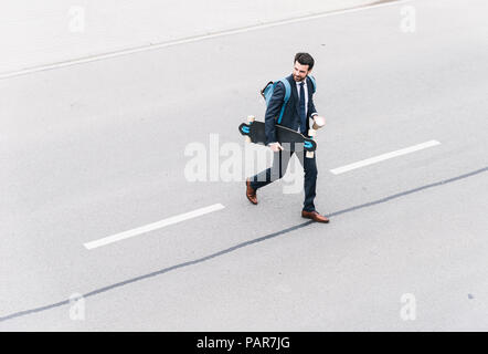 Geschäftsmann mit Takeaway Kaffee und Skateboard zu Fuß auf der Straße Stockfoto