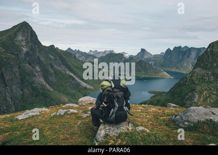 Norwegen, Lofoten, Moskenesoy, Mann sitzt auf einem Felsen, mit Blick über Kjerkefjord Stockfoto