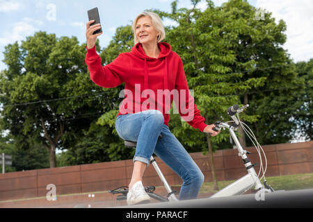 Ältere Frau mit City Bike mit Handy Stockfoto