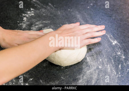 Frau Vorbereitung Pizza Teig auf schwarzem Granit Tisch Stockfoto
