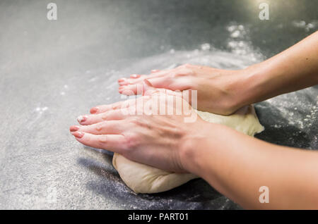 Frau Vorbereitung Pizza Teig auf schwarzem Granit Tisch Stockfoto