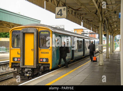 Diesel S-Bahn neben einer Plattform in Cardiff Central Station. Ein Treiber ist in die Kabine und eine Person zieht einen Koffer entlang der Plattform Stockfoto