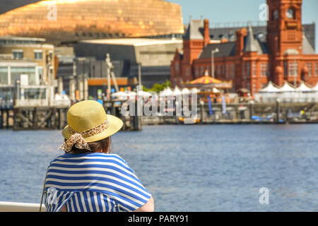 Frau mit Sonnenhut lehnte sich auf Geländer über Cardiff Bay in Richtung Wahrzeichen am Wasser. Stockfoto