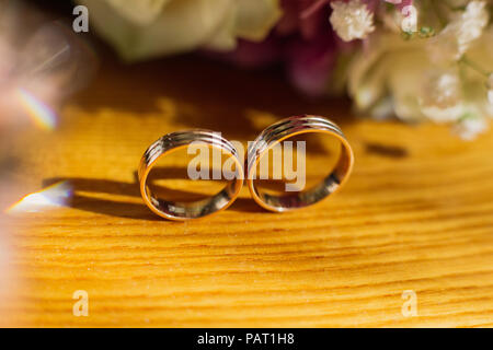 Schöne getonten Bild mit Hochzeit Ringe liegen auf einem Holz- Oberfläche vor dem Hintergrund der einen Blumenstrauß. Stockfoto