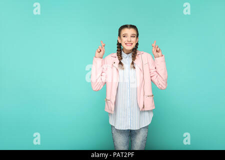 Hoffnungsvoller Wunsch Portrait von schönen süße Mädchen stehend mit Make-up und Frisur in braunen Zopf gestreift Hellblau shirt rosa Jacke. Indoor, Studio Stockfoto