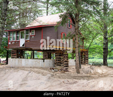 Ein braunes Holz Fachwerkhaus auf einem Riverfront bis für den Bau eines neuen Betonfundament aufgebockt. Stockfoto