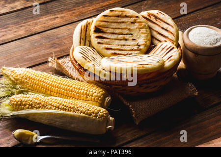 Blick vom hohen Winkel der rustikalen Tisch mit mehreren Boden mais Arepas, einige Mais und Butter. Venezolanische und Kolumbianische traditionelles Essen Stockfoto