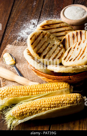 Blick vom hohen Winkel der rustikalen Tisch mit mehreren Boden mais Arepas, einige Mais und Butter. Venezolanische und Kolumbianische traditionelles Essen Stockfoto