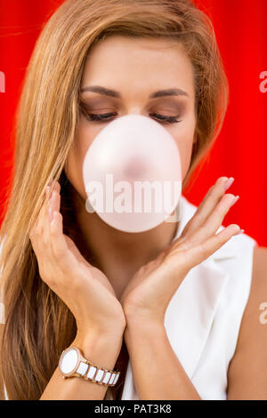 Lustige Portrait von schönen jungen cute woman in white Mode Anzug sehen blasen Bubble Gum gegen industrielle Rote Wand. Urban Style Girl, schnelle lifestyl Stockfoto