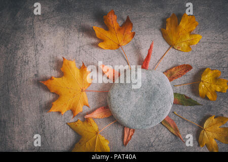 Getrocknete Herbstliche Blätter in rot-gelben Farben um Stein in floralen Komposition arrangiert auf scratchy Hintergrund Stockfoto