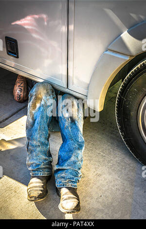 Ein Mechaniker unter Lkw tragen Cowboy Stiefel & dirty Jeans nur von der Taille abwärts außerhalb der Garage in New Mexiko gesehen Stockfoto