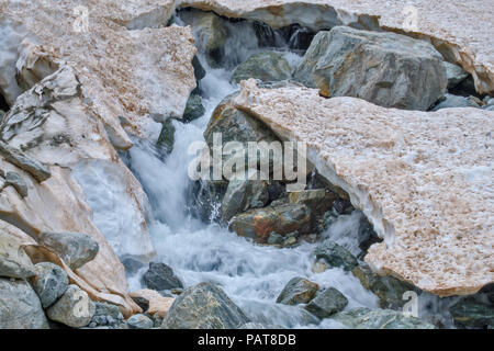 Gletscherbach an Ablation zone von Sofia Gletscher, die durch die Steine und durch Braun schmelzende Schnee an der Spitze der Arkhyz Bergen umgeben Stockfoto