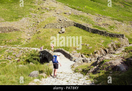 Wanderer Wandern auf Fußweg über Stockley Brücke in den Bergen des Lake District National Park im Sommer. Seathwaite, Cumbria, England, Großbritannien, Großbritannien Stockfoto