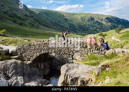 Biker überfahrt Stockley Brücke mit Wanderer ruht auf Wand in Lake District National Park. Seathwaite Borrowdale Cumbria England Großbritannien Großbritannien Stockfoto