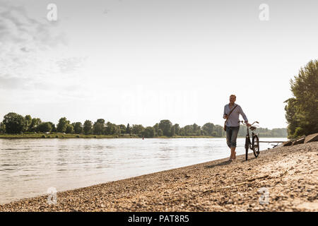 Reifer Mann mit Fahrrad mit an Rhein Ufer smartphone Stockfoto