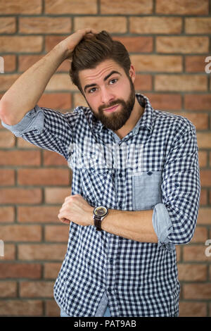 Portrait von bärtigen jungen Mann vor der Wand den Kopf kratzen Stockfoto