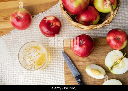 Blick von oben auf die Reife saftige Äpfel und Glas cidre Trinken auf rustikalen Holztisch. Glas selbstgemachten Apfelwein und lokal angebaute Bio Apfel, geschossen von ab Stockfoto