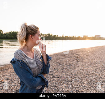 Junge blonde Frau wartet auf flußufer am Abend Stockfoto