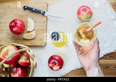 Blick von oben auf die Reife saftige Äpfel und Glas cidre Trinken auf rustikalen Holztisch. Sicht der Hand Glas selbstgemachten Apfelwein und lokal wachsen Stockfoto