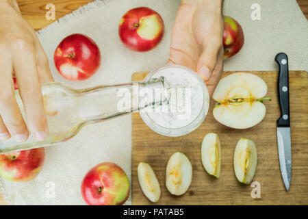 Gießen Sekt apple Cidre trinken in Glas, Ansicht von oben. Flach Bild mit den Händen zur Festsetzung ein Getränk von Apfelwein auf rustikalen Holztisch Hintergrund mit RIP Stockfoto