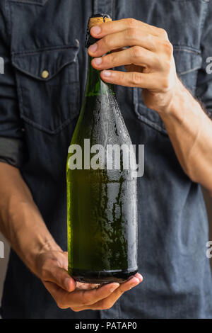 Männliche Hand verkorkt Flasche premium Cidre. Schöne Eis kalte Flasche Apfelwein in die Hände des Menschen Stockfoto