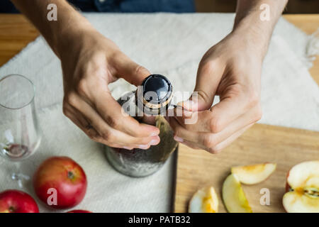 Blick von oben auf die männlichen Händen öffnen Flasche premium Cidre. Von oben geschossen von Entkorken schöne Eis kalte Flasche Apfelwein, lokal reifer Apfel angebaut Stockfoto
