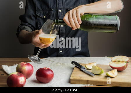 Männliche Hände gießen Premium cidre Wein Glas über rustikalen Holztisch. Man gießt ein Glas vintage apple Wein aus Eis kalte Flasche Stockfoto