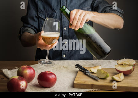 Männliche Hände gießen Premium cidre Wein Glas über rustikalen Holztisch. Tasting vintage Apple Cider aus Eis kalte Flasche Stockfoto