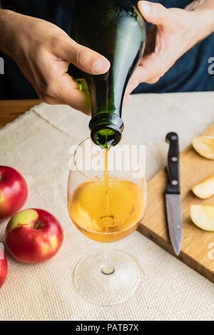 Blick von oben auf die Menschen gießen premium Cidre aus Glas. Nahaufnahme der männlichen Händen gießen Vintage apple Wein in schönes Glas im rustikalen Tisch Hintergrund mit Stockfoto