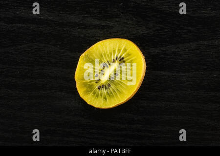 Eine Scheibe frischen Golden Brown Kiwi sungold Vielzahl flatlay auf schwarzem Holz Stockfoto