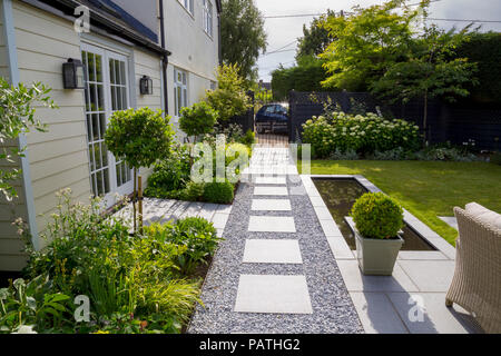 Blick auf London Stein Granit Pflastersteine in Richtung Eingangstor, mit Blumenrabatten, pool Wasser und Viburnum tinus Formgehölze Stockfoto