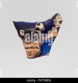 Glas cameo Cup (scyphus) Fragment. Kultur: Roman. Abmessungen: Insgesamt: 1 3/4 x 2 1/4 in. (4,5 x 5,7 cm). Datum: Ende 1.Jh. v. Chr. - Mitte des 1. nachchristlichen Jahrhundert. Transluzente Kobaltblau mit Deckweiß Overlay. Körper Fragment der große Tasse mit Untere vorstehendes Teil der angewandten. Auf außen, unten frontal Leiter der Satyr Griff, mit Haaren in Büscheln über Stirn und zu Seiten mit entsprechenden Links spitzes Ohr, markanten Augenbrauen, breite flache Nase und gespitzten Lippen; rechts von der Griff, Panflöte aus grünen Laub ausgesetzt. Gebrochen mit verwitterten Kanten und Vertiefungen der Oberfläche blasen, Abstumpfung und patch Stockfoto