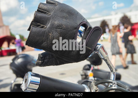 Schwarz Leder Handschuh oder mitt auf dem Lenker eines Motorrads geparkt außerhalb der Stadt in der Nähe zu sehen. Stockfoto