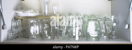 Verschiedene Gläser in einem weißen Schrank auf dem Regal. Banken, Krüge, Gläser, Becher. Stockfoto