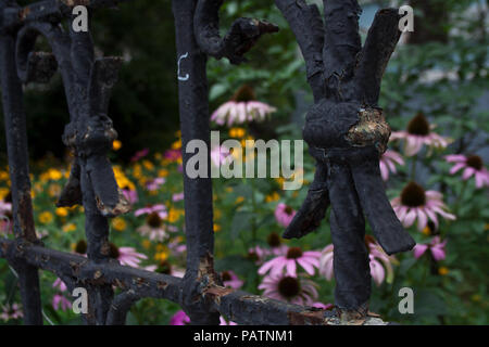 Schäbig Metallzaun Details in Schwarz lackiert mit rosa und gelbe Blumen hinter