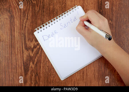 Die Mädchen schreiben einen Brief an den Weihnachtsmann auf dem Holztisch. Weibliche Hand die Feder oben Leere notepad mit Text Lieber Santa Stockfoto