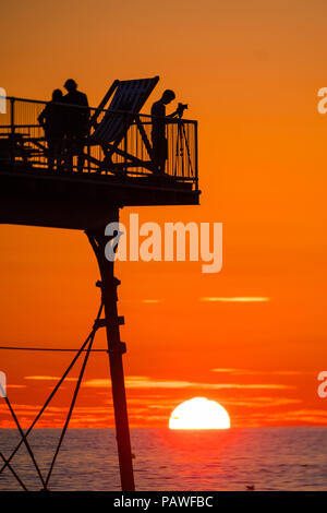 Aberystwyth Wales UK, Mittwoch, 25. Juli 2018 UK Wetter: die Menschen werden durch den herrlichen Sonnenuntergang über Aberystwyth Pier Silhouette am Ende eines Tages des heißen Sommer Sonnenschein. Großbritannien große Hitzewelle fort, mit wenig Erholung von der sehr trockenen Wetter trotz etwas Regen in der Prognose für das Wochenende Foto: Keith Morris/Alamy leben Nachrichten Stockfoto