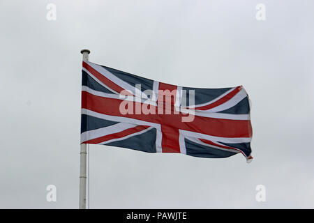 Union Jack Flagge im Wind flattern auf einem weißen Fahnenmast mit einem grauen Himmel Hintergrund. Stockfoto