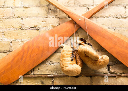 Alte Vintage Paddel und Boxhandschuhe hängen an einer Wand Freiliegender Ziegel Stockfoto