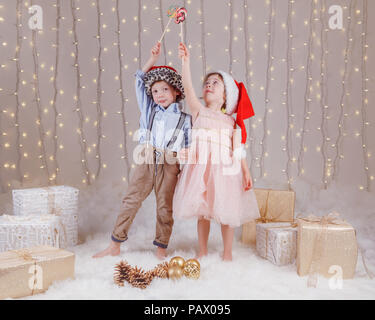 Portrait von weissen Kaukasischen Kinder Freunde tragen Santa Claus Hüte, Weihnachten oder Neujahr. Kleine süße Mädchen und Jungen essen Lutscher in Stockfoto