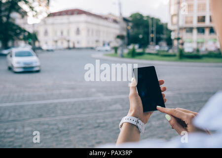 Rückansicht unkenntlich junge Frau mit Smart Phone in der Nähe von europäischen Pflasterstein Straße mit Autos. Close-up weibliche Hände berühren Gerät Geröll Stockfoto