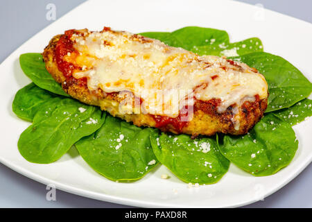 Chicken Parmesan auf einem Bett aus Spinat mit einer Prise frischem Parmesan Käse oben auf eine weisse Platte Stockfoto