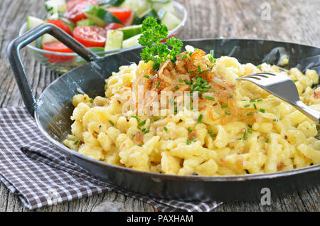 Süddeutschen Käse Nudeln mit gebratenen Zwiebeln in einer Pfanne mit Salat Stockfoto